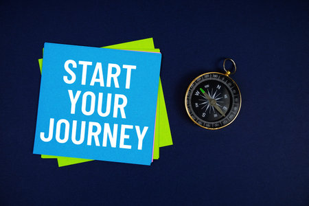 Start Your Journey text written on sticky note with compass on blue  background