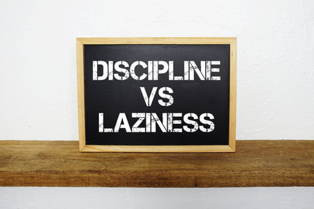 Discipline vs Laziness text written on blackboard with wooden shelf and concretebackgroundの写真素材