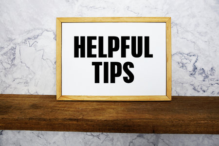 Blackboard with text "Helpful Tips" on a wooden shelf, set against a marble wall.の写真素材