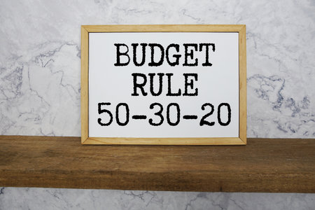50-30-20 Budget Rule , 50% Needs, 30% Wants, 20% Savings text written on whiteboard with wooden shelf and marble backgroundの写真素材