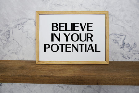Believe In Your Potential text written on whiteboard with wooden shelf and marble backgroundの写真素材