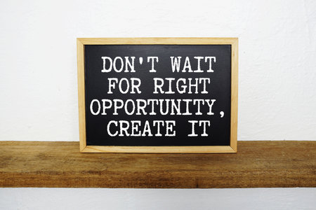 Don't wait for Right Opportunity, Create It text written on blackboard with wooden shelf and concrete backgroundの写真素材
