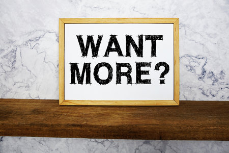 Want More? text written on whiteboard with wooden shelf and marble backgroundの写真素材