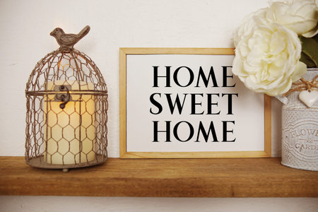 Home Sweet Home text written on whiteboard with candle light and bird cage on wooden shelfの写真素材