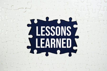 Jigsaw puzzle with a missing piece with "Lessons Learned" on blue backgroundの写真素材