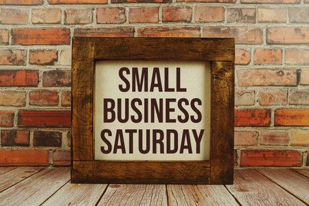 Small Business Saturday text written on wooden board standing with old brick wall background
