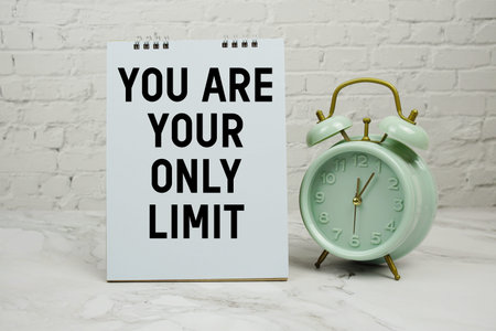 You Are Your Only Limit with green vintage alarm clock against a white brick wall background.