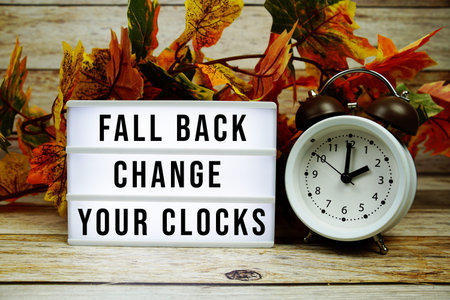 Fall back change your clocks text with alarm clock and maple leaf decoration on wooden background