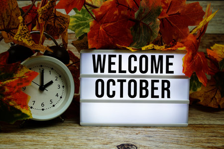 Welcome October text with alarm clock and maple leaf decoration on wooden backgroundの写真素材