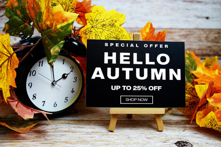 Hello Autumn Sale 25% off Special Offer text with alarm clock and maple leaf decoration on wooden backgroundの写真素材