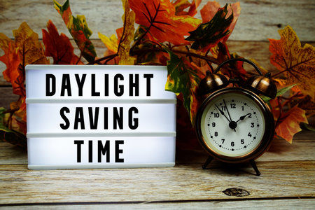 Daylight Saving Time text with alarm clock and maple leaf decoration on wooden backgroundの写真素材