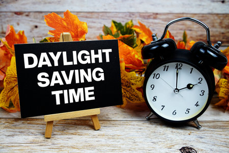 Daylight Saving Time text with alarm clock and maple leaf decoration on wooden backgroundの写真素材