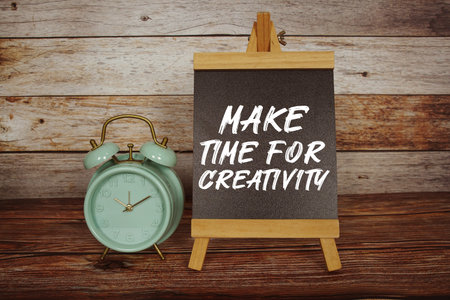 Make Time For Creativity text on easel blackboard with alarm clock on wooden background