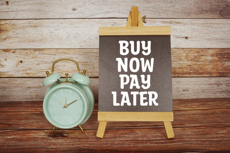 Buy Now Pay Later text on easel blackboard with alarm clock on wooden background