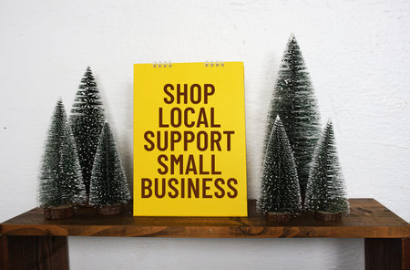 A bright yellow sign with the message Shop Local Support Small Business sits on a wooden shelf,...