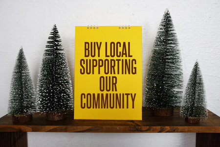 A bright yellow sign with the message Buy Local Supporting Our Community sits on a wooden shelf,...