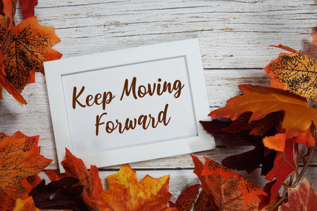 Keep Moving Forward text with maple leaf decoration on wooden background