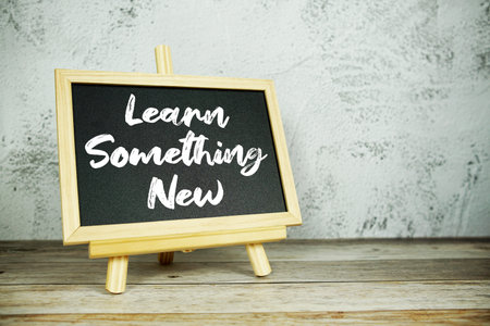 wooden easel displays a blackboard with the bold white text Learn Something New set against a rustic...