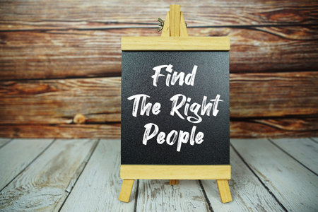 wooden easel holds a blackboard with the white text Find the Right People set against a rustic...