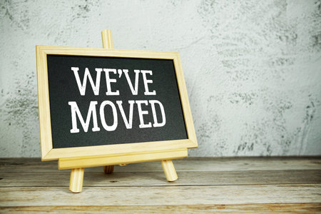 wooden easel displays a blackboard with the bold white text "We have moved" set against a rustic wooden surface and textured gray wall backgroundの写真素材
