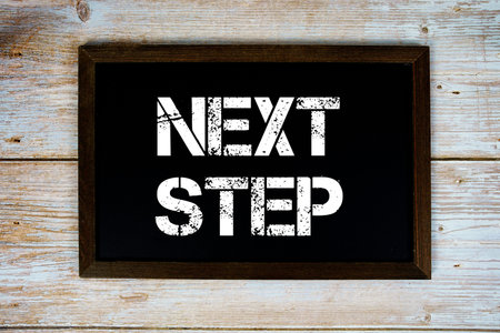 Next Step text on blackboard on wooden background