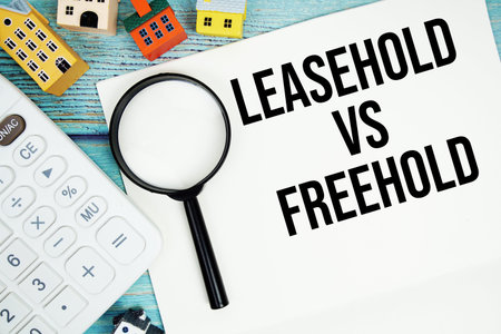Notepad with Leasehold vs Freehold with Calculator, magnifying glass and house model on wooden...