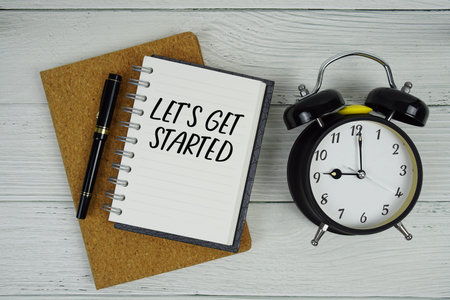 Let's Get Started text written on notepad with alarm clock on wooden background