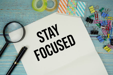 Stay Focused text written on notepad with magnifying glass flat lay on wooden backgroundの写真素材