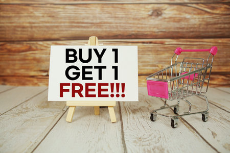 Buy 1 Get 1 Free!!! on sign board with Mini Shopping Cart on Wooden Backgroundの写真素材