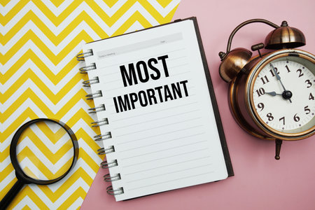 Most Important text written on notepad with alarm clock and magnifying glassの写真素材