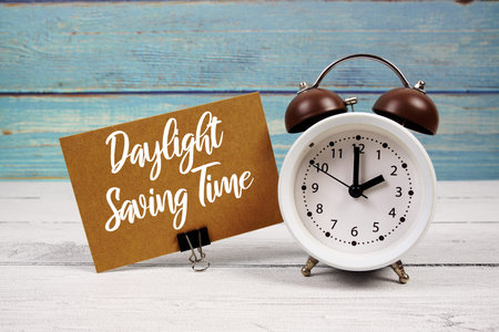 Daylight Saving Time  text written on paper card with alarm clock on wooden backgroundの写真素材