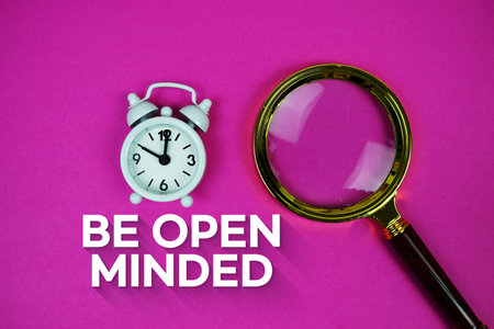 Alarm clock and a magnifying glass on a bright pink background, with text "Be Open Minded"の写真素材