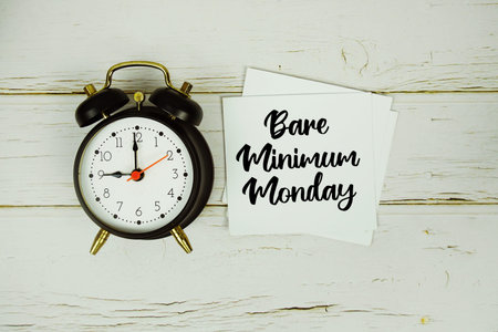Bare Minimum Monday text message on paper with alarm clock on wooden background