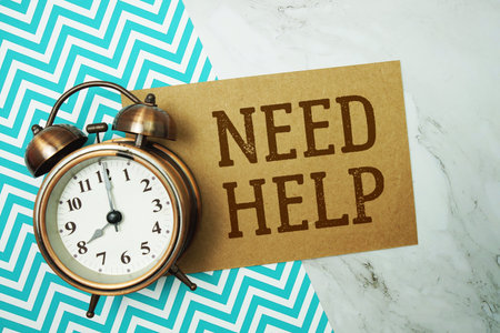Need Help text written on paper card with alarm clock on marble background