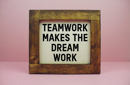 Wooden framed with motivational quote TEAMWORK MAKES THE DREAM WORK displayed against a pink...