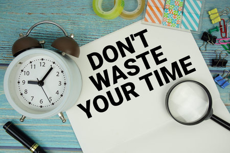 Don't Waste Your Time text written on notepad with alarm clock and magnifying glass flat lay on...