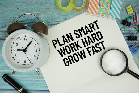 Plan Smart. Work Hard. Grow Fast text on a paper surrounded by office supplies, a magnifying glass,...