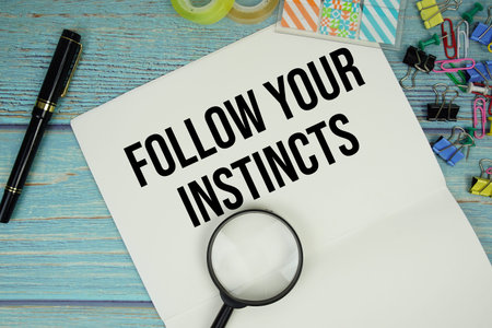 Follow Your Instincts text on a paper surrounded by office supplies and magnifying glass on a blue...