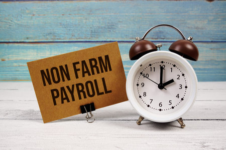 Non Farm Payroll text written on paper card with alarm clock on wooden background