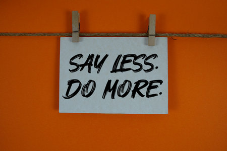 Say Less Do More text written on paper card with rope and wooden clip hanging
