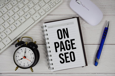 On-page SEO text with alarm clock, keyboard and wireless mouse on wooden background