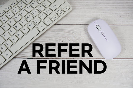 Refer A Friend text with keyboard and wireless mouse on wooden background