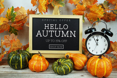 Autumn Sale 15% text with alarm clock and maple leaf decoration on wooden background
