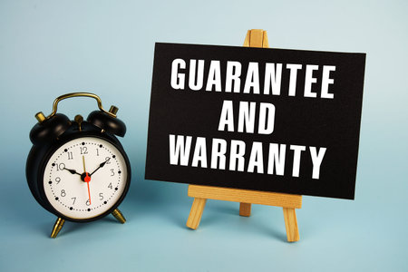 Guarantee And Warranty text with easel and alarm clock on blue background