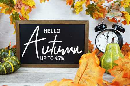 Autumn Sale 45% text with alarm clock and maple leaf decoration on wooden background