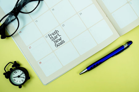 Fresh Start, New Goals message written on calendar date with alarm clock, glasses and magnifying glass on yellow background