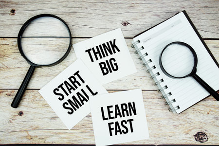 Think Big, Start Small, Learn Fast text written on paper card with magnifying glass on wooden background