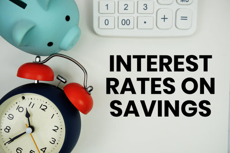Interest Rates On Savings text written notepad with calculator, piggy bank and alarm clock on white background