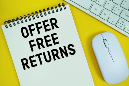 Notepad with the text Offer Free Returns and white keyboard and wireless mouse on yellow background