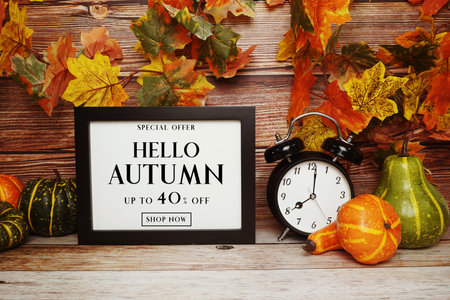 Hello Autumn Sale 40% off text with alarm clock and maple leaf decoration on wooden background